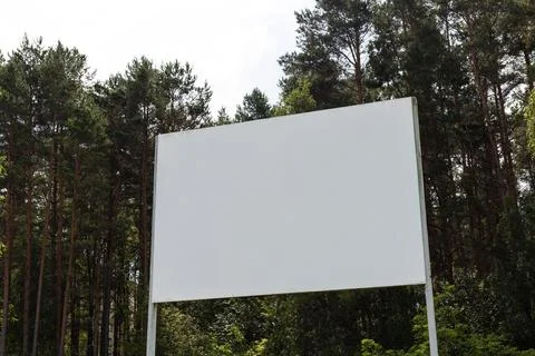 A large empty billboard is set against a backdrop of tall trees in a peaceful Stock Photos
