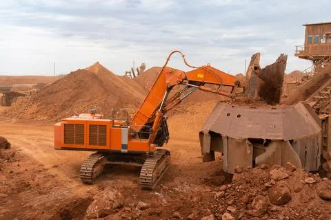 A large excavator loads rock into a crusher with a bucket Stock Photos