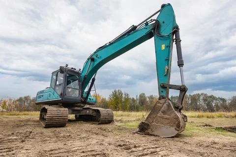 A large excavator operates in an open field, digging into the dirt on a cloud Stock Photos