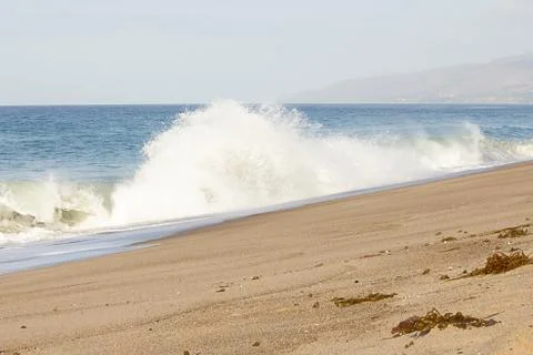 Large exploding splashing spray from wave on sandy beach, with open ocean Stock Photos