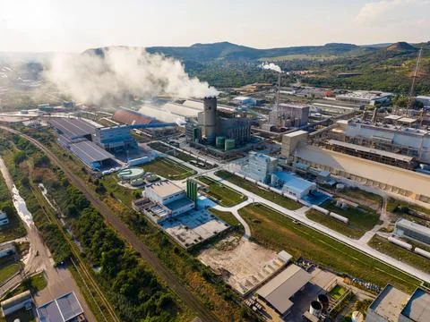 A large factory complex is located in a rural area. Smoke rises from stacks a Foto stock