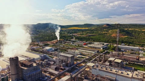 Large factory with smoke rising above buildings and green hills in the Stock Footage 340881069