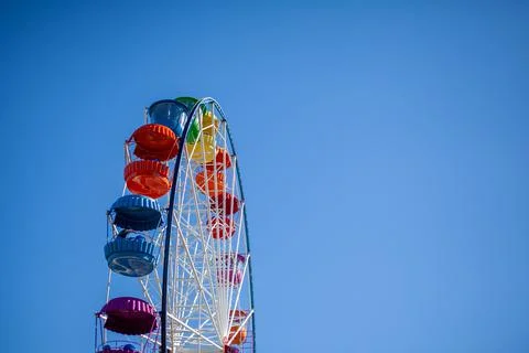A large Ferris wheel against a blue sky. Booths with people go up. Stock Photos