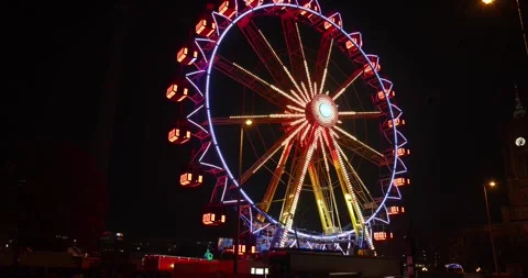 A large ferris wheel in changing colored lights spins at a Christmas market Stock Footage 256095915