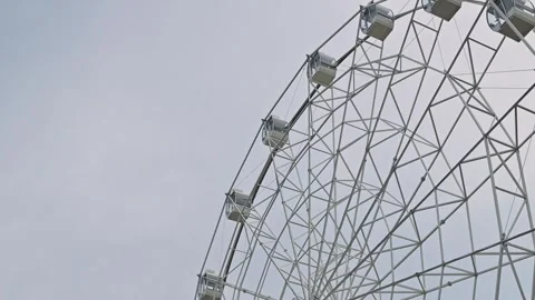 A large ferris wheel stands tall against a cloudy sky, with an emphasis on its Stock Footage 344527627