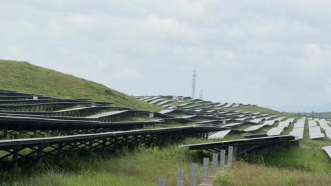 A large field of solar panels spans rolling ground as soft clouds glide above Stock Footage 323438972