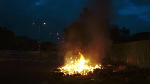 Large fire burns on place of car wreck leftovers on urban road edge at night Stock-Footage 315438618