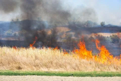 A large fire on the side of the road with bright flames and smoke on a dry .. Stock Photos