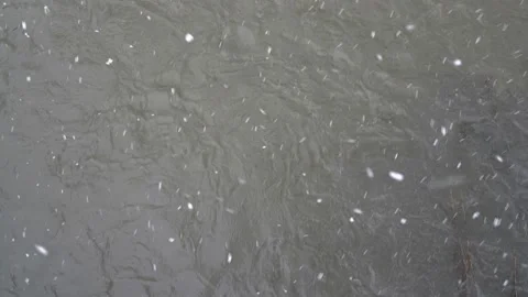 Large flakes of snow fall on the surface of a stormy river on a gloomy winter 스톡 동영상 141869155