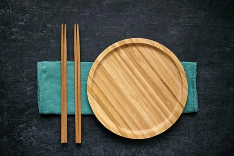 Large flat empty bamboo plate and chopsticks lie on green linen napkin Stock Photos