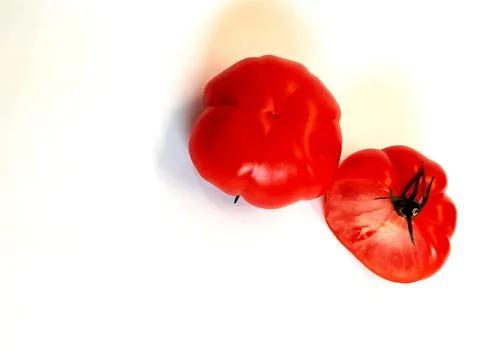 A large flat tomato and a second one cut in half, shot from above Stock Photos
