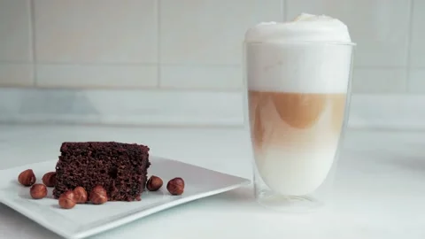 Large foamy latte coffee next to brownie with nuts on marble countertop Stock Footage 131006902