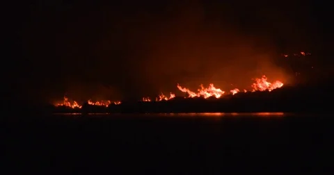 Large forest gorse fire and smoke reflected in lake water at night Stock Footage