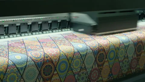 Large-format printer moves across colorful patterned fabric. Print head advan Stock Footage 331863353