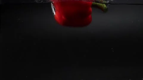 A large fresh red bell pepper falls into the water with splashes, slowly sinking Stock Footage 133353909