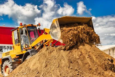 A large front loader pours sand into a pile at a construction site. Transport Photos