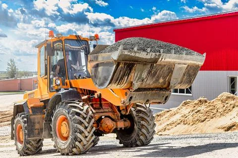 A large front loader transports crushed stone or gravel in a bucket at a cons Stock Photos