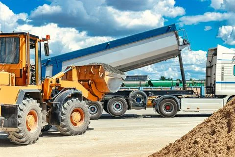 A large front loader transports crushed stone or gravel in a bucket at a cons Photos