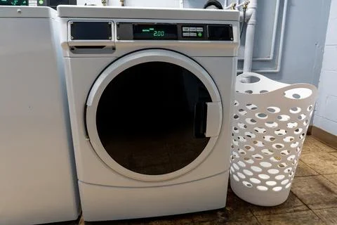 Large front-loading washing machine with a laundry basket beside it Foto stock