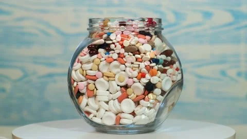 A large glass jar full of various pills rotates on a bluish background. Stock Footage 131332601