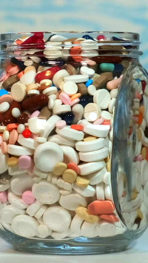 A large glass jar full of various pills rotates on a bluish background. The.. Stock-Footage 291956477