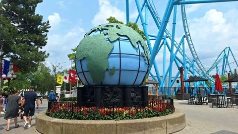 Large globe statue displayed in amusement park with roller coaster. Stock Photos