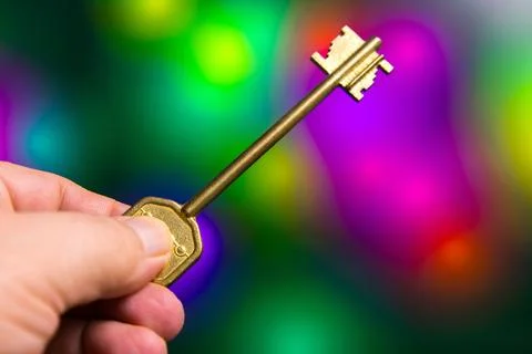 Large gold key held in hand against colorful blurred background showcasing light 스톡 사진