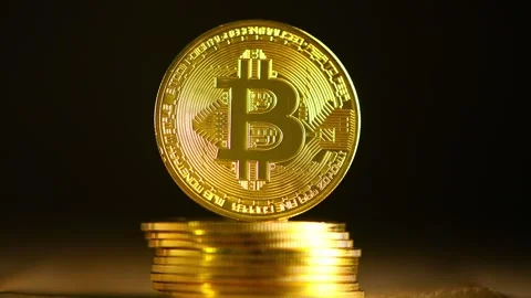 Large, golden physical bitcoin stands on a stack of bitcoins, representing Stock Footage 306571042