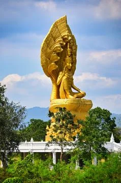 Large golden statue sits on a base in a green area with trees and mountains.. Stock Photos