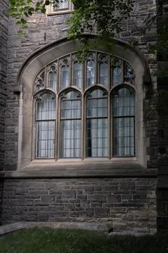 Large gothic arch window on historic stone building facade framed by green .. Stock Photos