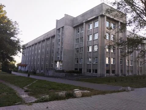 Large gray building on a background of blue sky and green trees Stock Photos