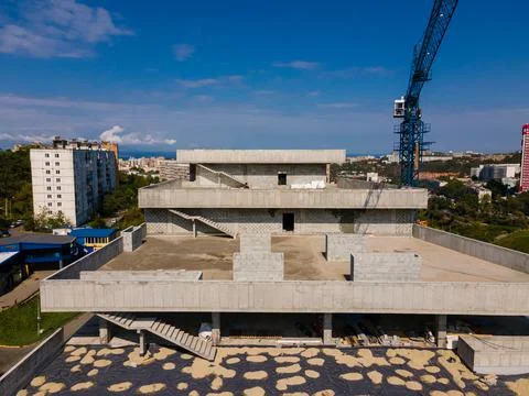 A large gray building under construction in the city. Blue construction crane Stock Photos