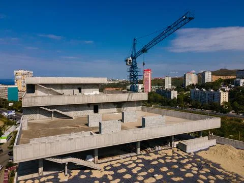 A large gray building under construction in the city. Blue construction crane Stock Photos