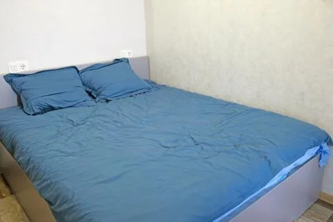 A large gray double bed is in the corner of a light gray room. The bed is cov Stock Photos