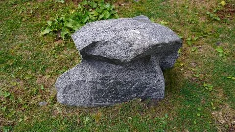 Large gray granite boulder split in two on green grass, yellow patches. Stock Photos