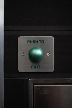 Large green button on door panel indicating push to exit in a buildings hallway Stock Photos