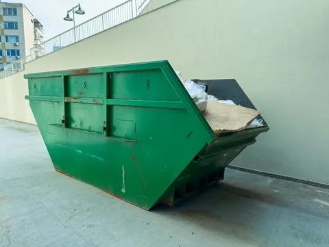 Large green dumpster located in a city alleyway filled with trash and debri.. Stock Photos