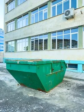 Large green dumpster placed by a building under clear sky in a city area Stock Photos