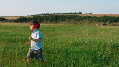 In a large green field cute little boy take his red headphones and listen music Stock Footage 170007953