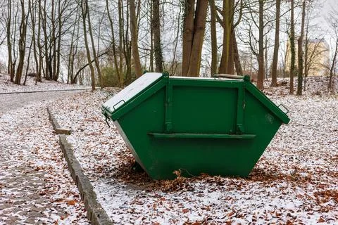 A large green garbage collection container in a city snow-covered park. Yel.. Stock Photos