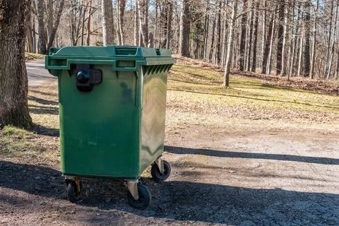 A large green garbage container on wheels, placed on a dirt. 스톡 사진
