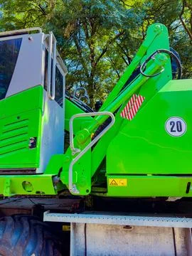 Large green machine works on a construction site beside trees during daytim.. Stock Photos