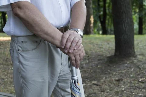 The large hands of an elderly man are folded on a cane with a watch on his ri Stock Photos