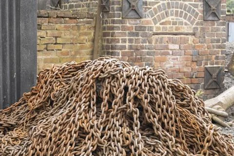 A large heap of rusty chains in front of a classic red brick wall with metal  Stock Photos