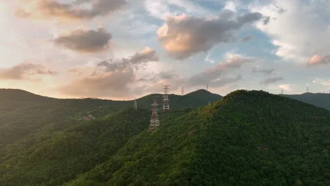 A large high-voltage transmission tower sits atop a hill and a lush green forest Video stock 314352524