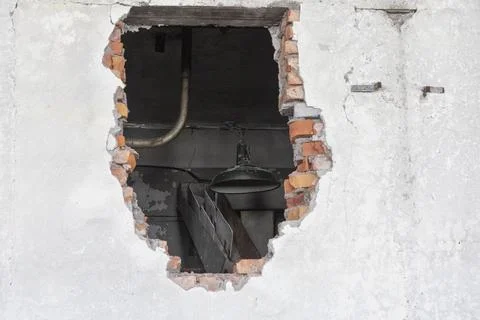 Large hole in an old brick wall. There's a lantern hanging behind the wall Fotos Stock