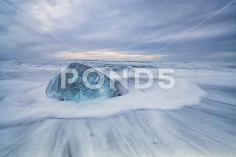 Large ice block laying on the shores of Southern Iceland while waves crash on sh Stock Photos