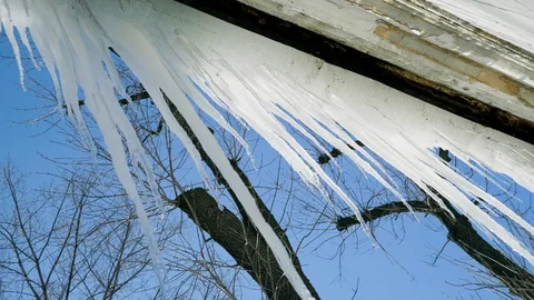 Large icicles melt in the sun rays against a clear blue sky. 4K Stockbeeldmateriaal 129737174