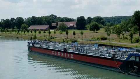 Large industrial cargo barge sailing down a scenic river canal surrounded b.. Видео 337292584