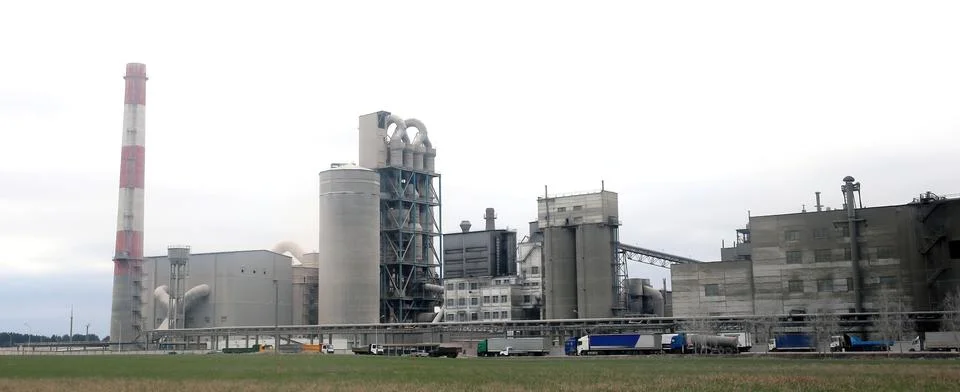 Large industrial complex features multiple structures and smokestack, with tr Stock Photos